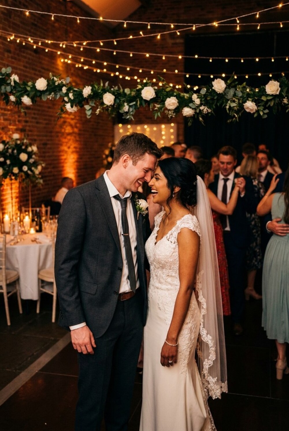 A newly married couple laughing together at the edge of the dancefloor under festoon lights